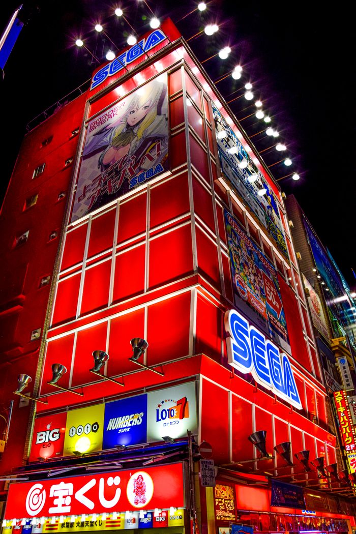 Bright lights and modern architecture of a Sega building in Tokyo's Akihabara district at night.