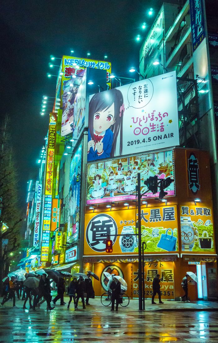 A vibrant nighttime street scene in Akihabara, Tokyo with colorful neon lights and anime billboards.